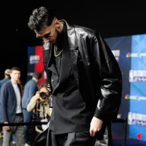 Man wearing a stylish black leather coat with a modern celebrity-inspired fashion look at a red carpet event.